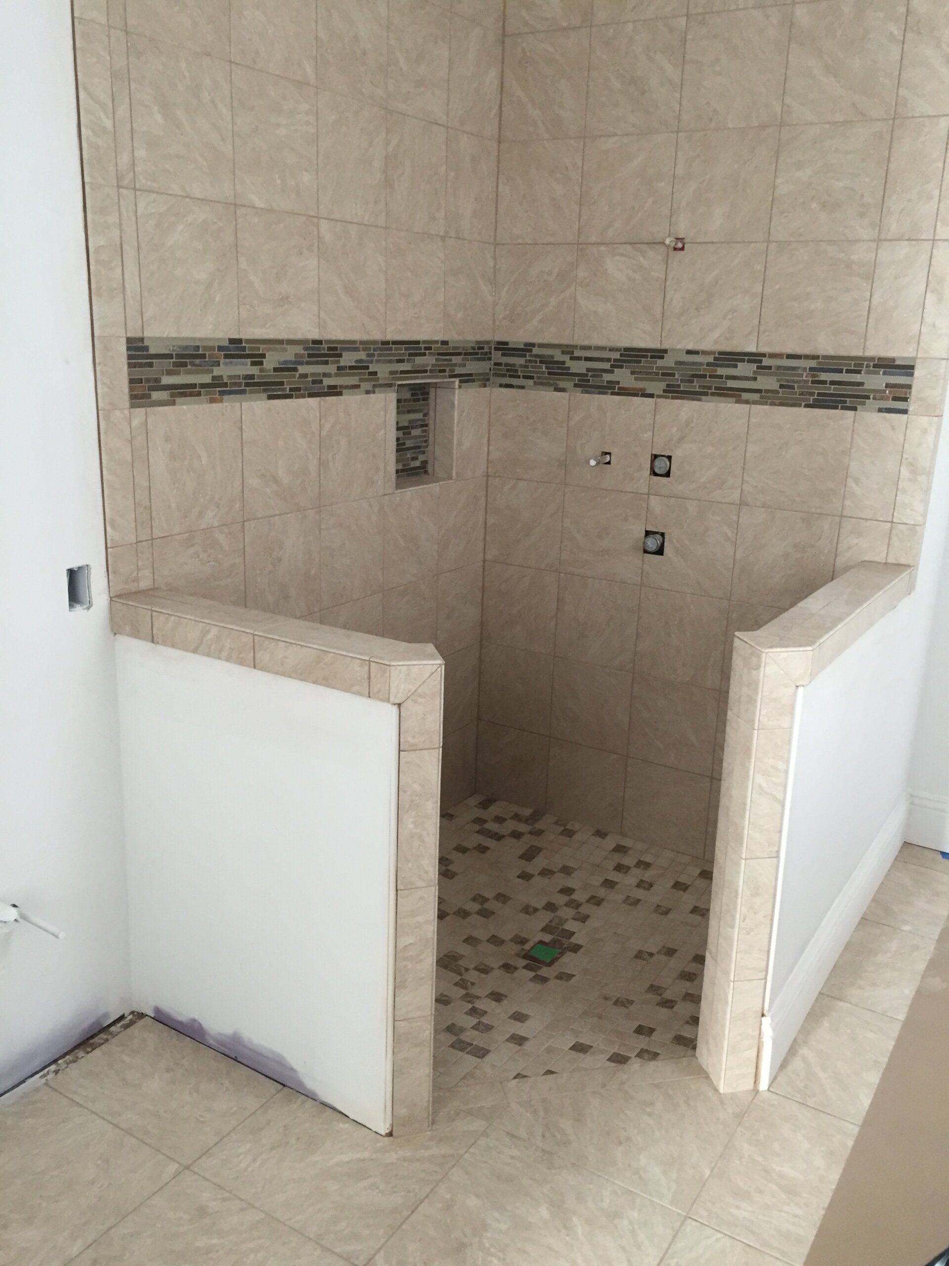 Shower under construction, beige tile walls and floor, mosaic tile accent, white partition walls.