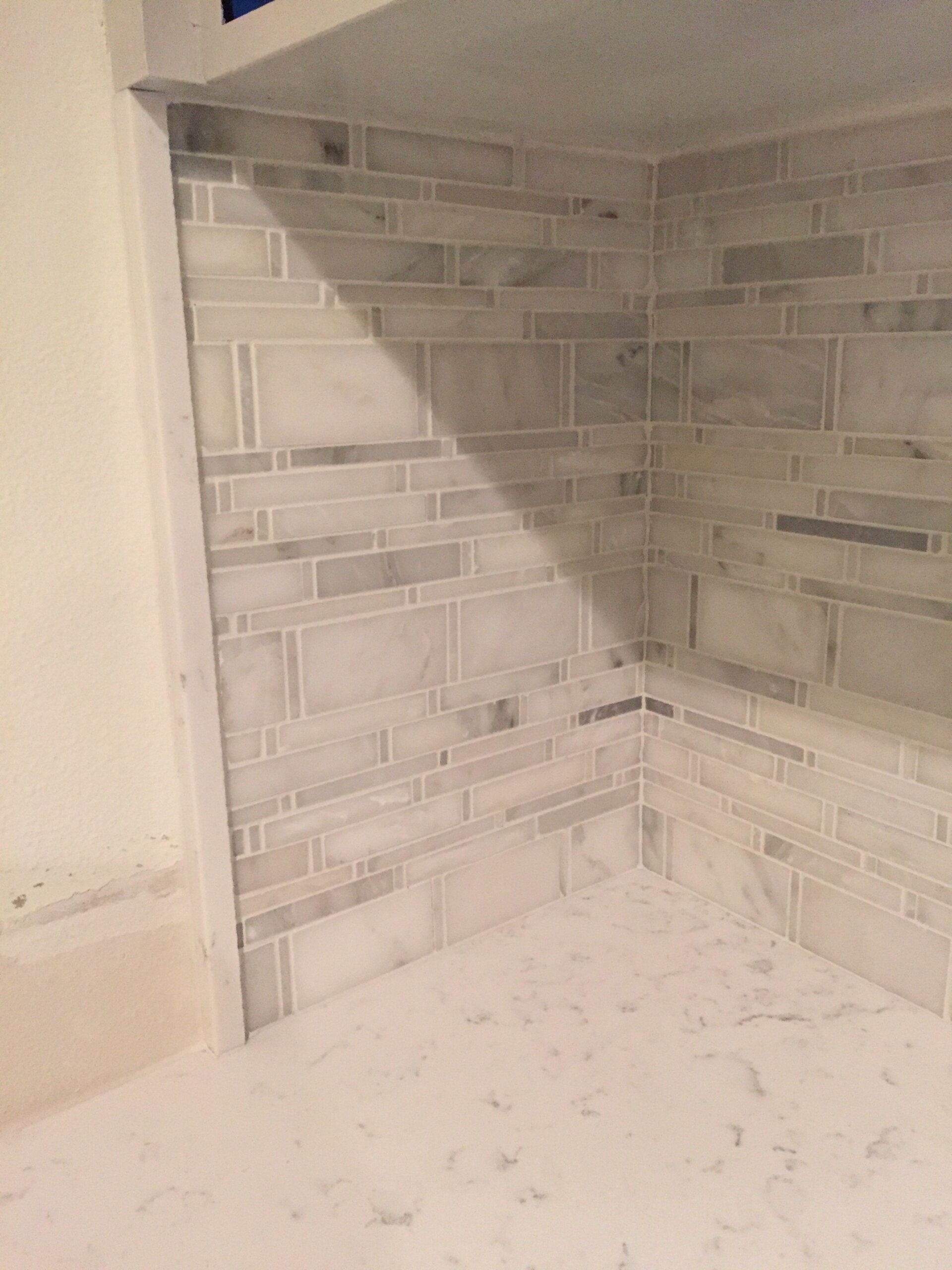 Bathroom corner with white and gray tiled walls. The floor is also tiled.