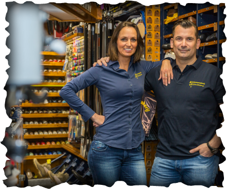Man en vrouw poseren in een winkel bij de schappen met artikelen. Vrouw in blauw shirt, man in zwart shirt, lachend.
