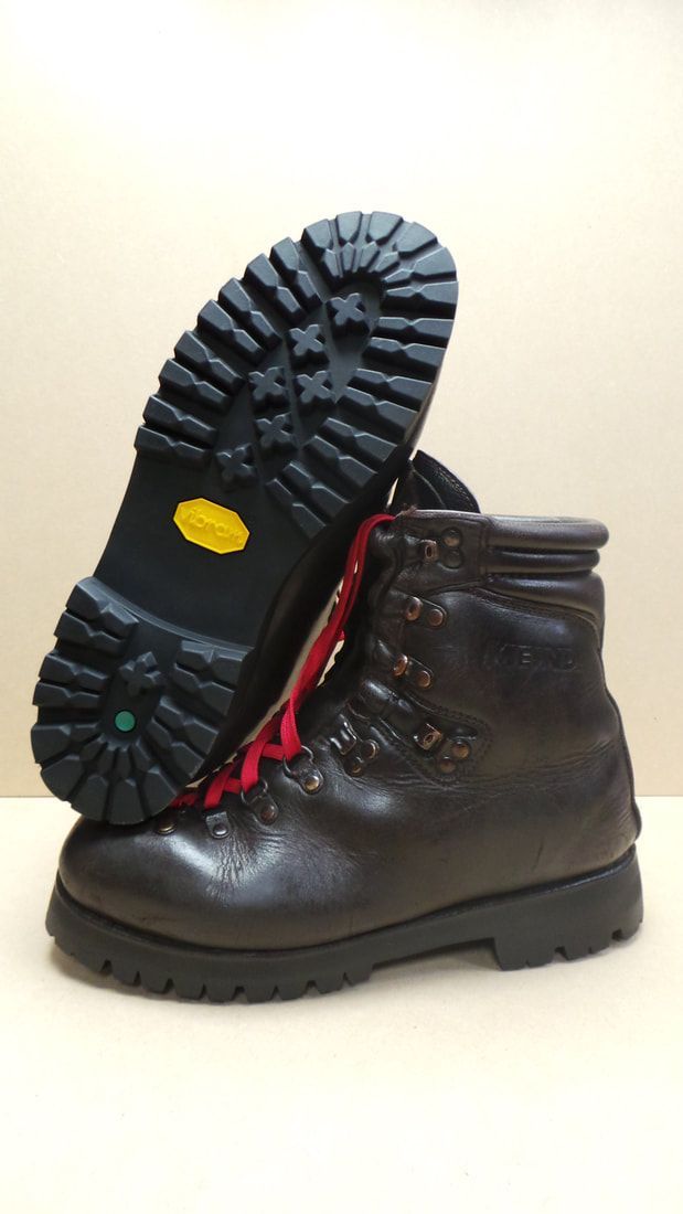 Donkerbruine leren wandelschoen, met rode veters, zool omhoog, met zichtbaar Vibram-profiel.