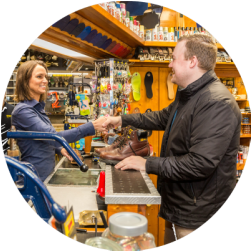 Une femme et un homme se serrant la main au comptoir d'un magasin de réparation de chaussures ; chaussures, outils et fournitures visibles.