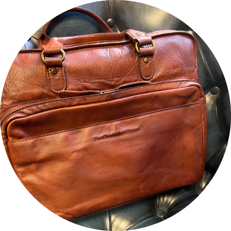 Bruine leren aktetas met handgrepen en voorvak, geplaatst op een donkere achtergrond.