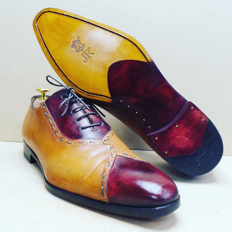 Bruine en bordeauxrode leren schoenen, één rechtopstaand en één waarvan de zool zichtbaar is.