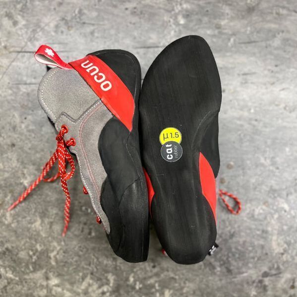 Twee OCUN klimschoenen. Eén toont de zool, maat 11,5, de andere de zijkant met rode veters en accenten.