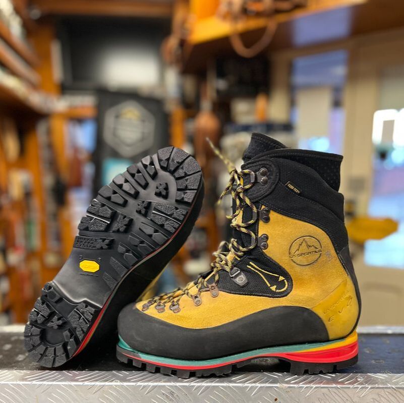 Gele en zwarte wandelschoenen met Vibram-zolen, tentoongesteld op een tafel binnen.