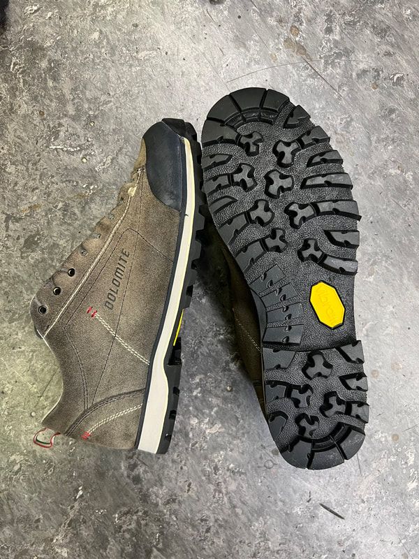 Grijze wandelschoen met zwart-gele zool, beide op een grijs oppervlak.