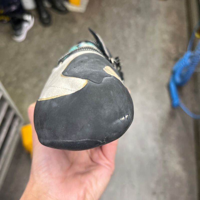 Close-up van de punt van een klimschoen in iemands hand. Er zijn slijtplekken op het rubber te zien.