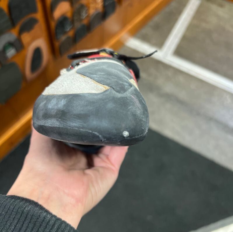 Close-up van een klimschoen, vastgehouden door een persoon, met een versleten, donkere rubberen neus.