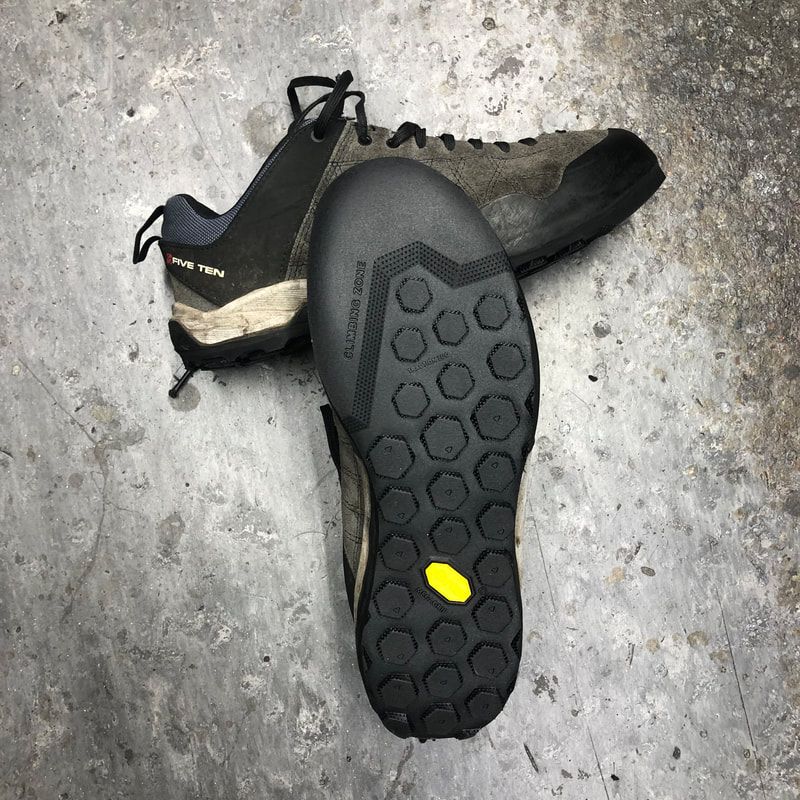 Een paar mountainbikeschoenen, zwarte Vibram-zool, grijs en zwart bovenwerk, op een betonnen ondergrond.