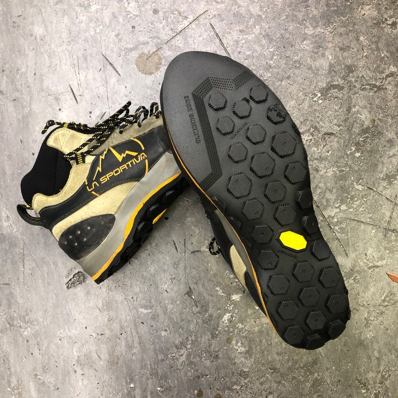 Wandelschoenen, donkere zool met zeshoekige zool, bovenkant bruin en zwart, op grijs beton.