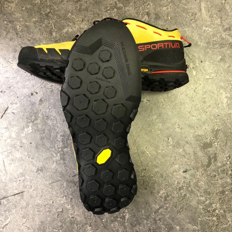 Geel-zwarte wandelschoenen met een geribbelde zool, op een betonnen ondergrond.