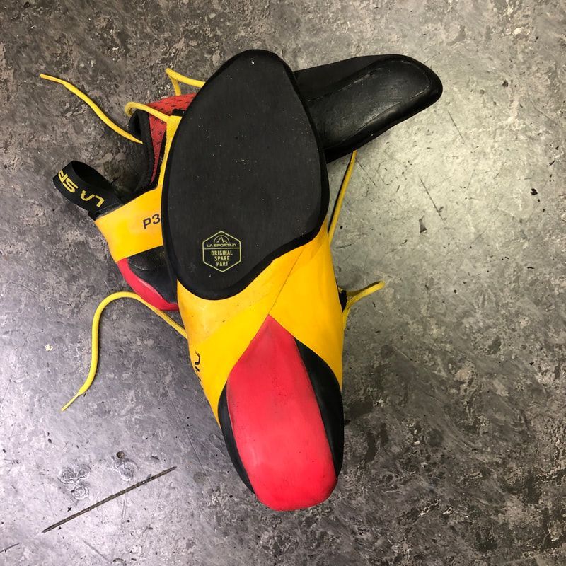 Een paar gele, rode en zwarte klimschoenen op een grijs betonnen oppervlak.