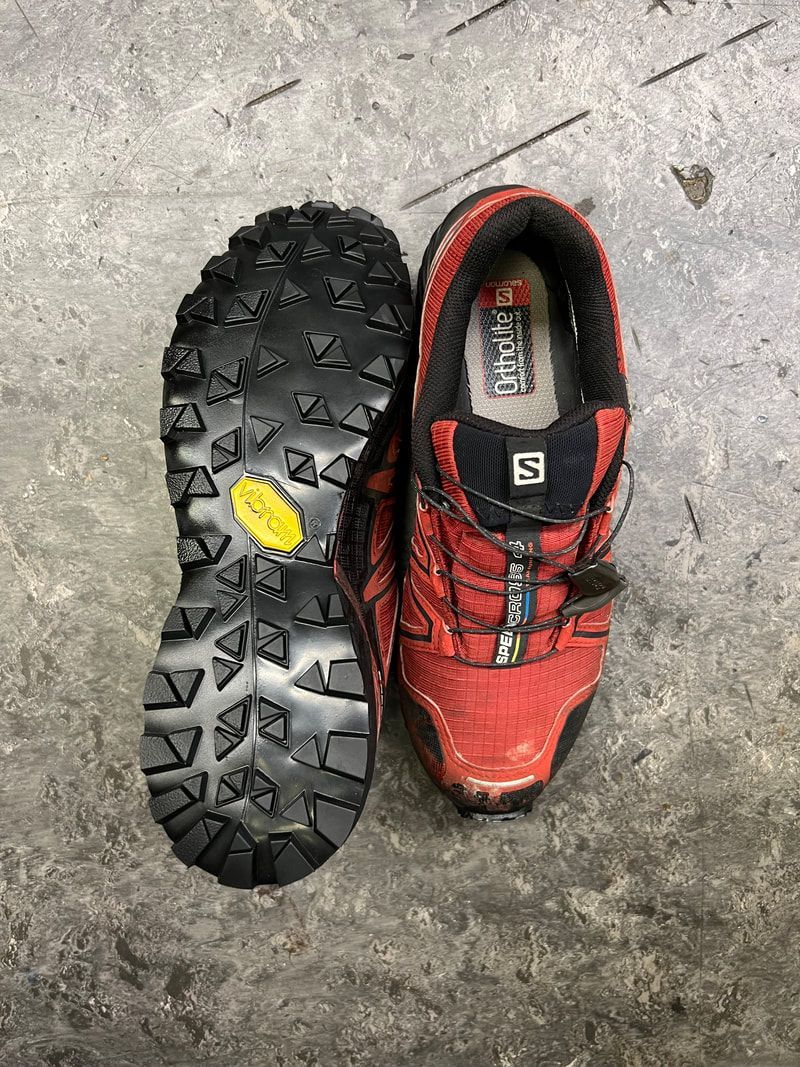 Rode en zwarte Salomon wandelschoen, zool omhoog, met Vibram-logo.
