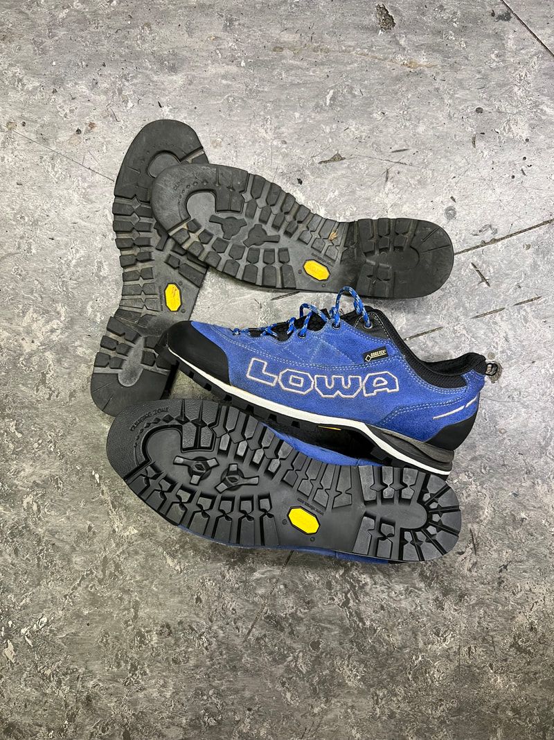 Blauwe en zwarte Lowa wandelschoenen met Vibram-zolen op een betonnen ondergrond.