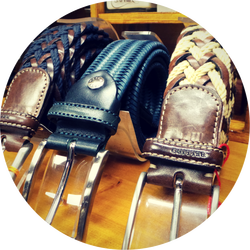 Trois ceintures en cuir tressé avec boucles en argent, présentées sur une étagère en bois.