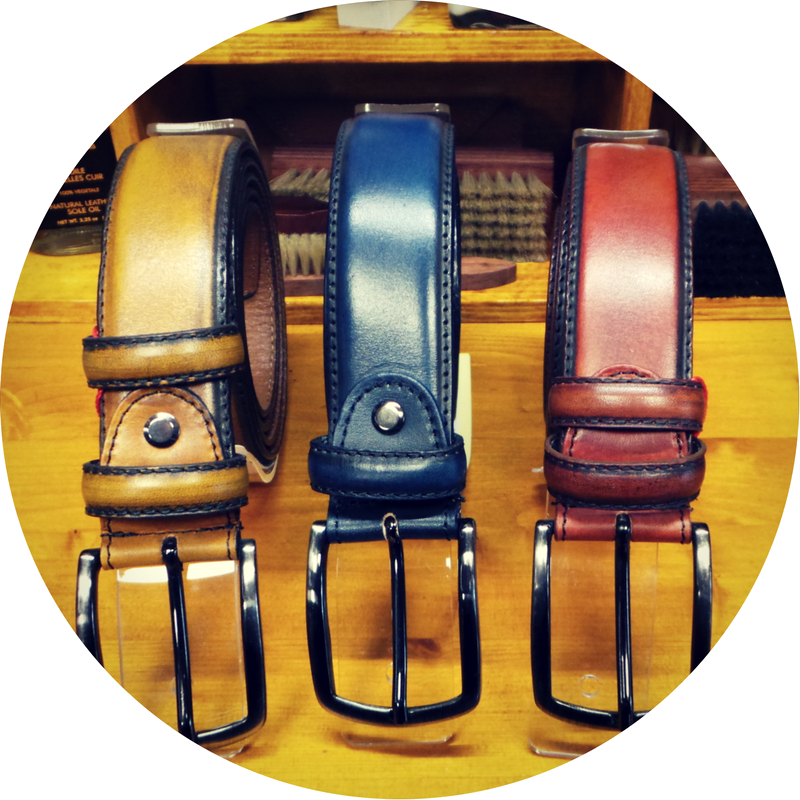 Drie leren riemen in bruin, blauw en rood met zilveren gespen liggen op een houten plank.