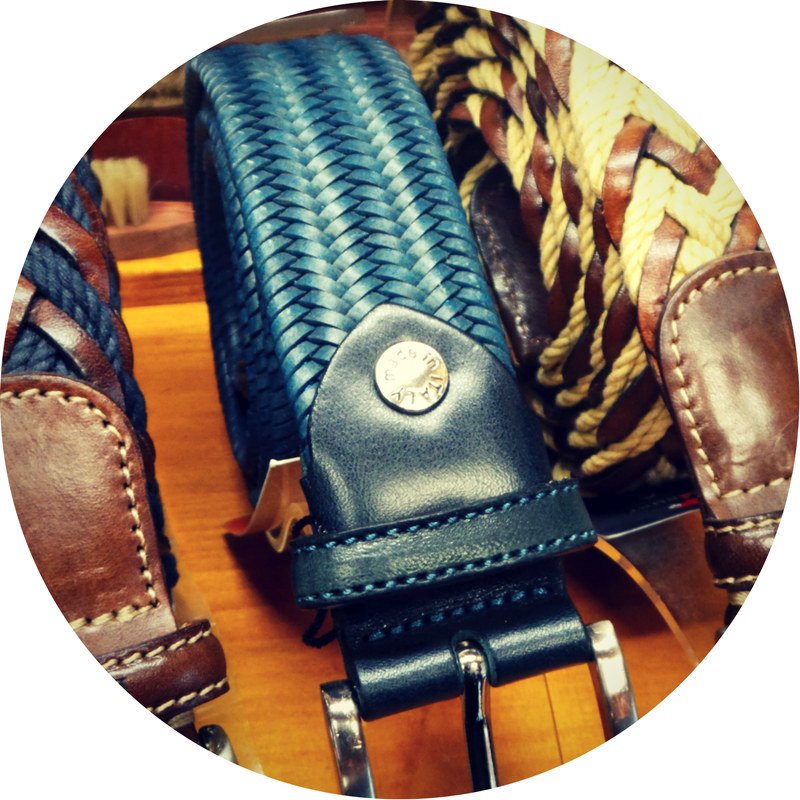 Close-up van een blauwe gevlochten leren riem met zilveren gesp, omringd door bruine en beige riemen.