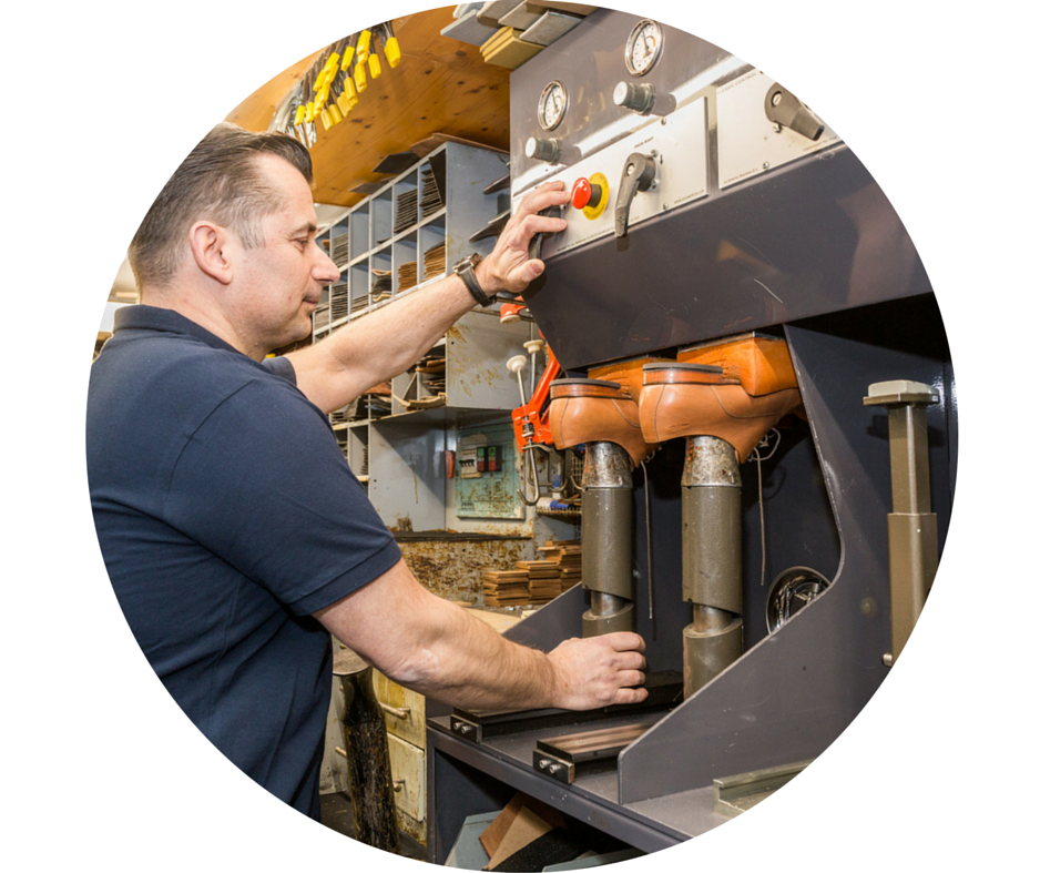 Schoenmaker gebruikt machines in een werkplaats. Man in een blauw shirt bedient apparatuur met bruine en grijze tinten.