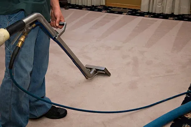 A man is cleaning a carpet with a vacuum cleaner.