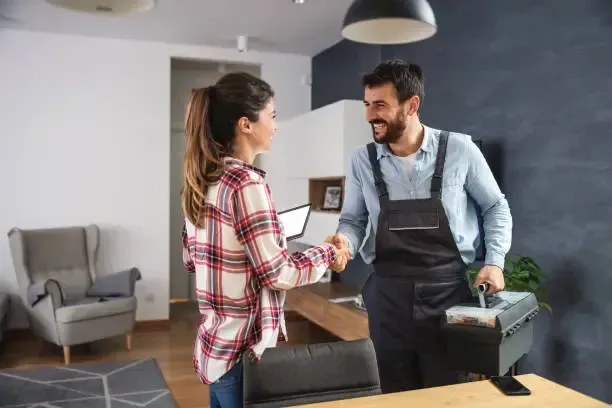 A professional from Ever Safe Pro and a woman shakes hands in a living room after providing a satisfactory cleanup service.