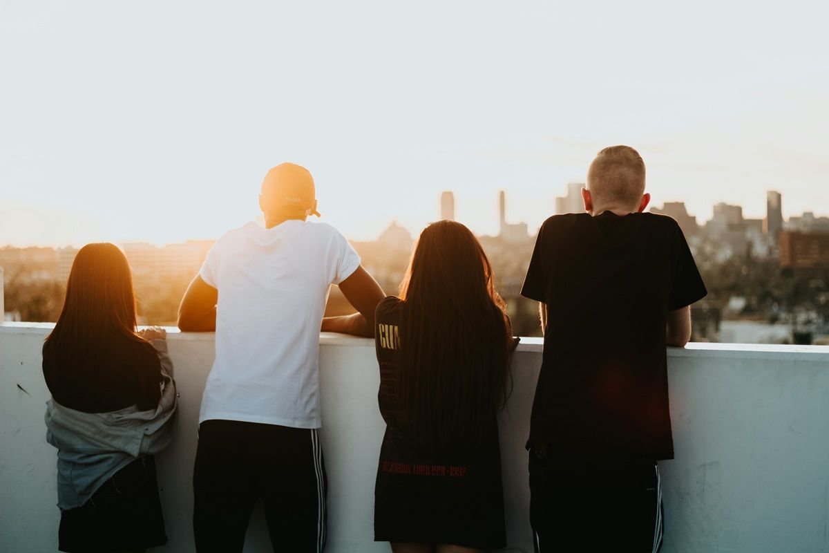 The back of four young people at sunset on a skyscraper rooftop