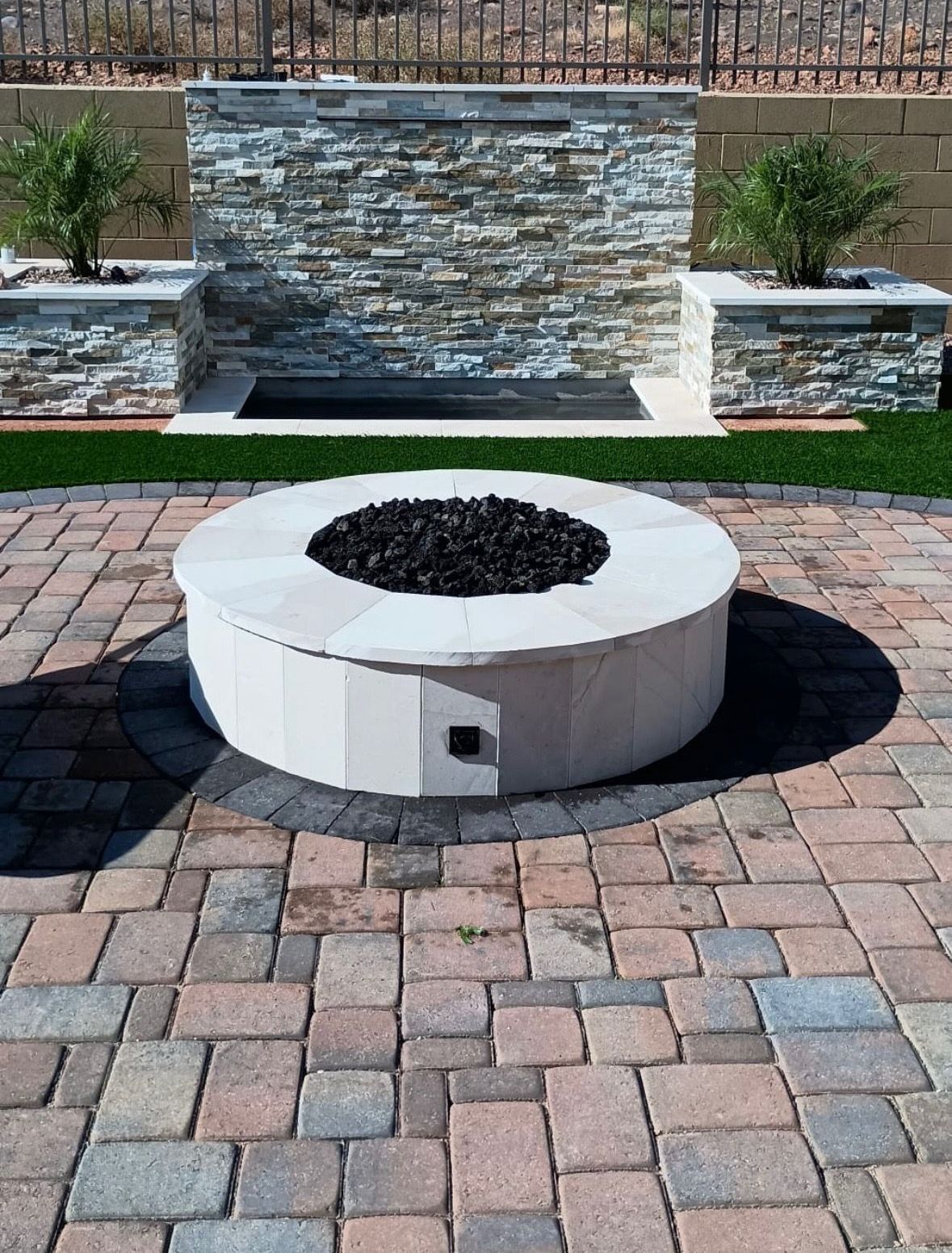 A fire pit is sitting on a brick patio next to a stone wall.
