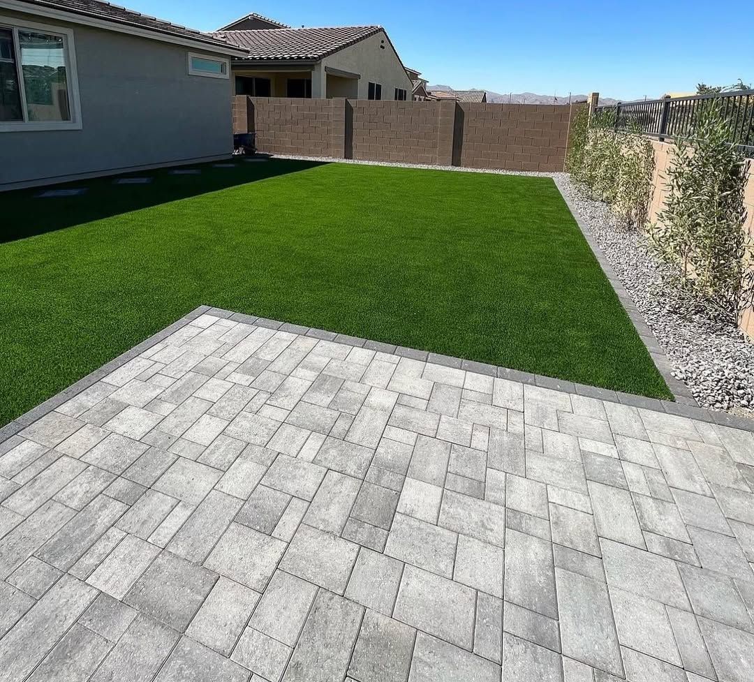 A backyard with a brick walkway and a lush green lawn.
