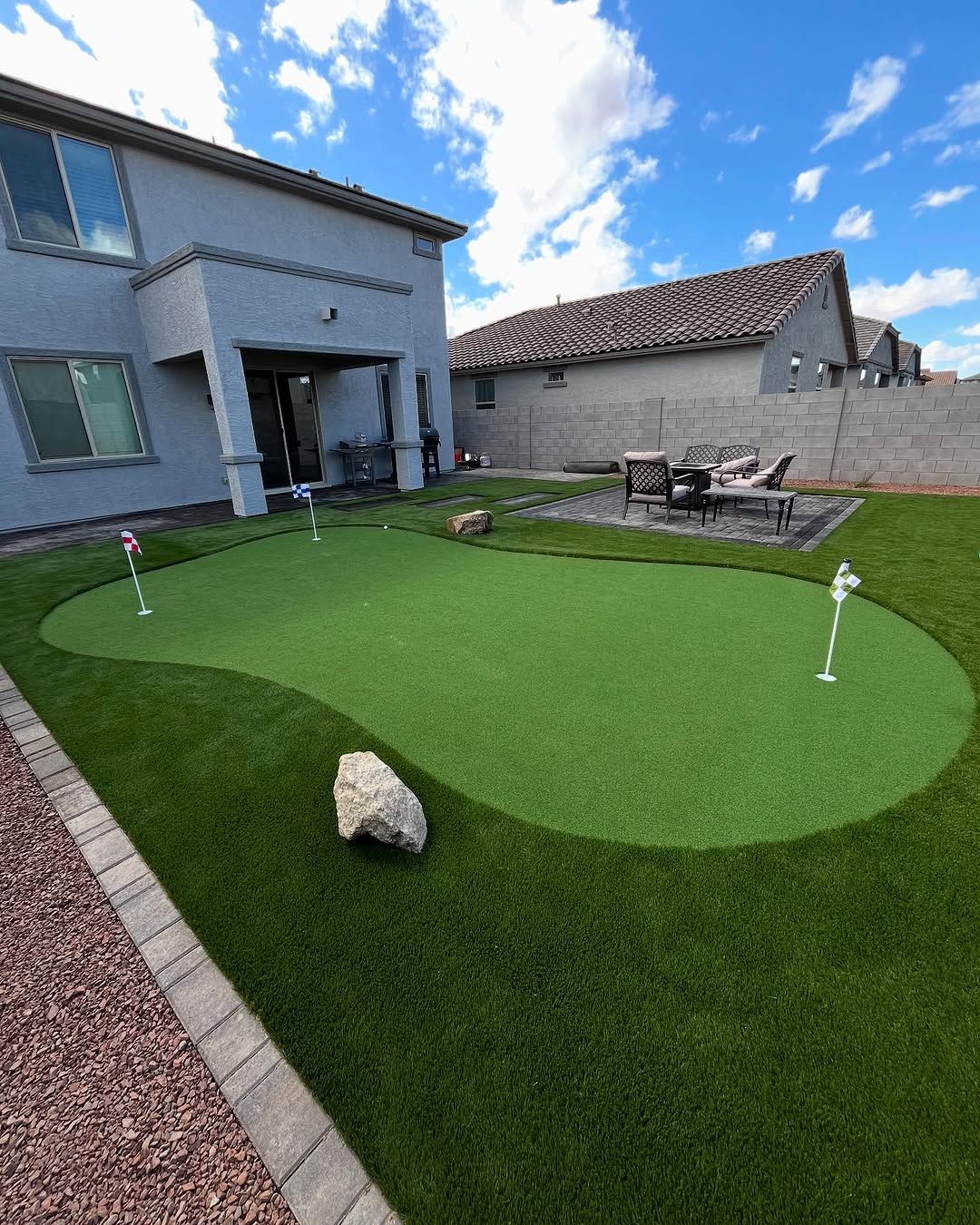 There is a putting green in the backyard of a house.