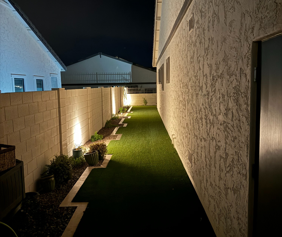 A backyard with a brick fence and a lush green lawn at night.