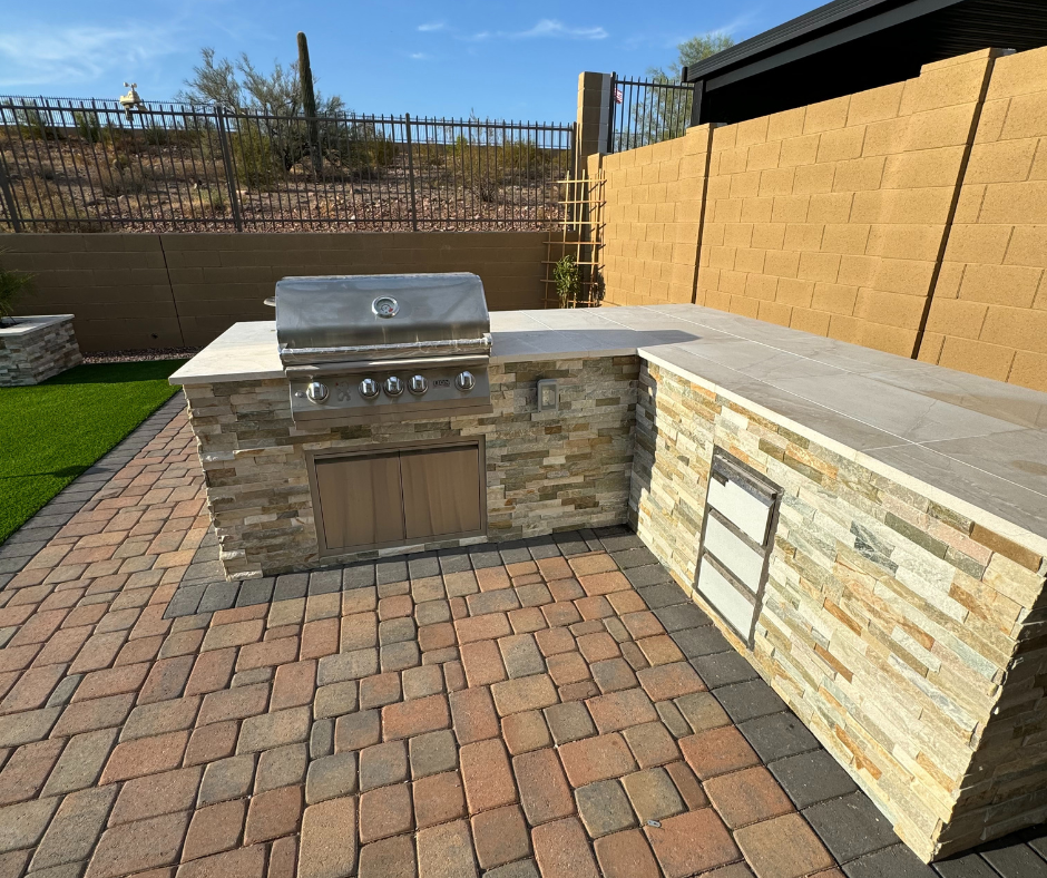 A grill is sitting on top of a stone counter in a backyard.