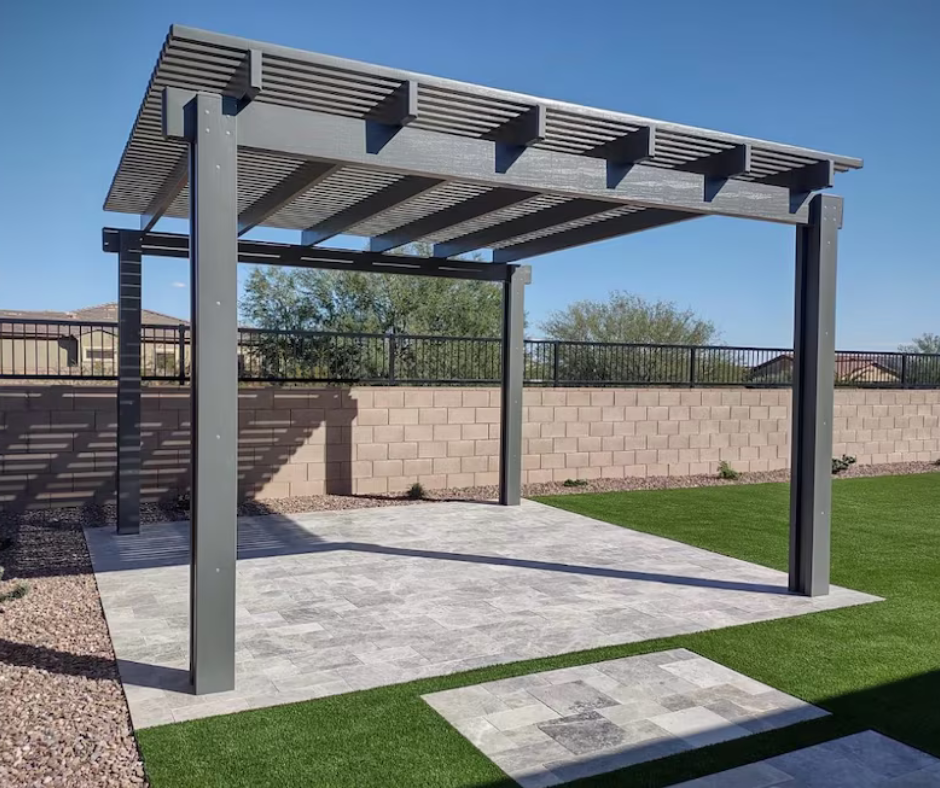 A pergola is sitting in the middle of a backyard next to a brick wall.