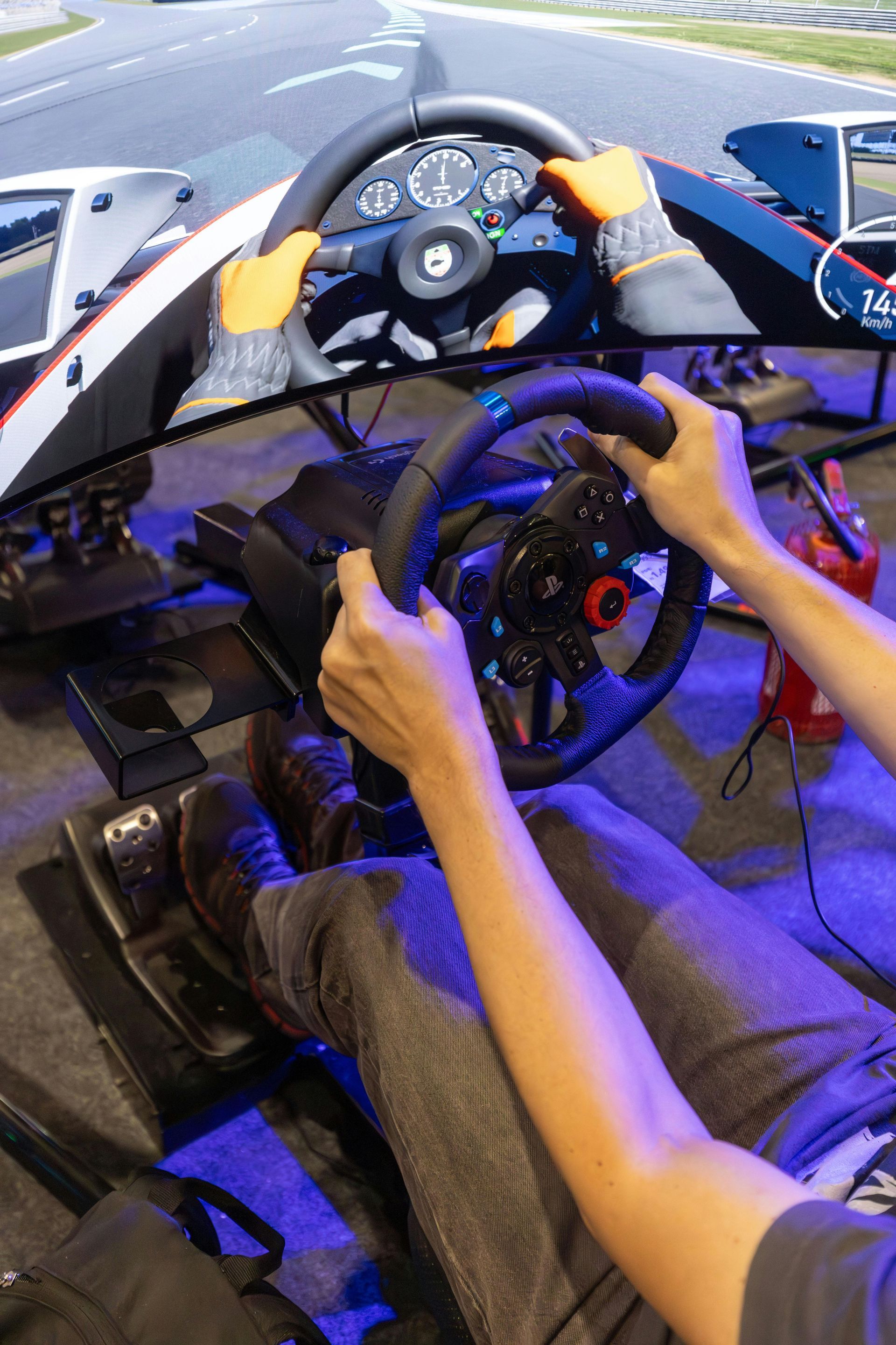 Person using a racing simulator, holding steering wheel with both hands, wearing gloves. Interior setting.