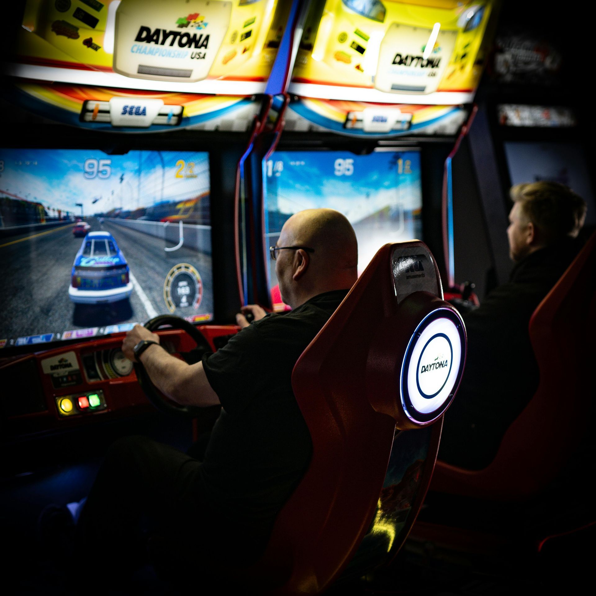 Two men playing Daytona arcade racing game.