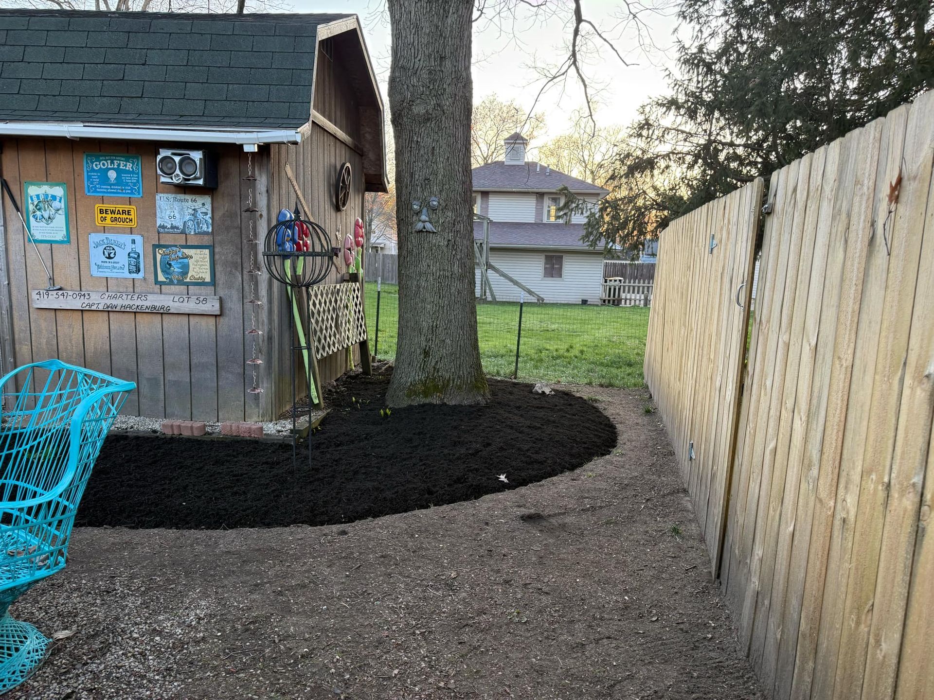 Backyard with a shed, a tree, mulch, and a fence. The ground is gravelly.