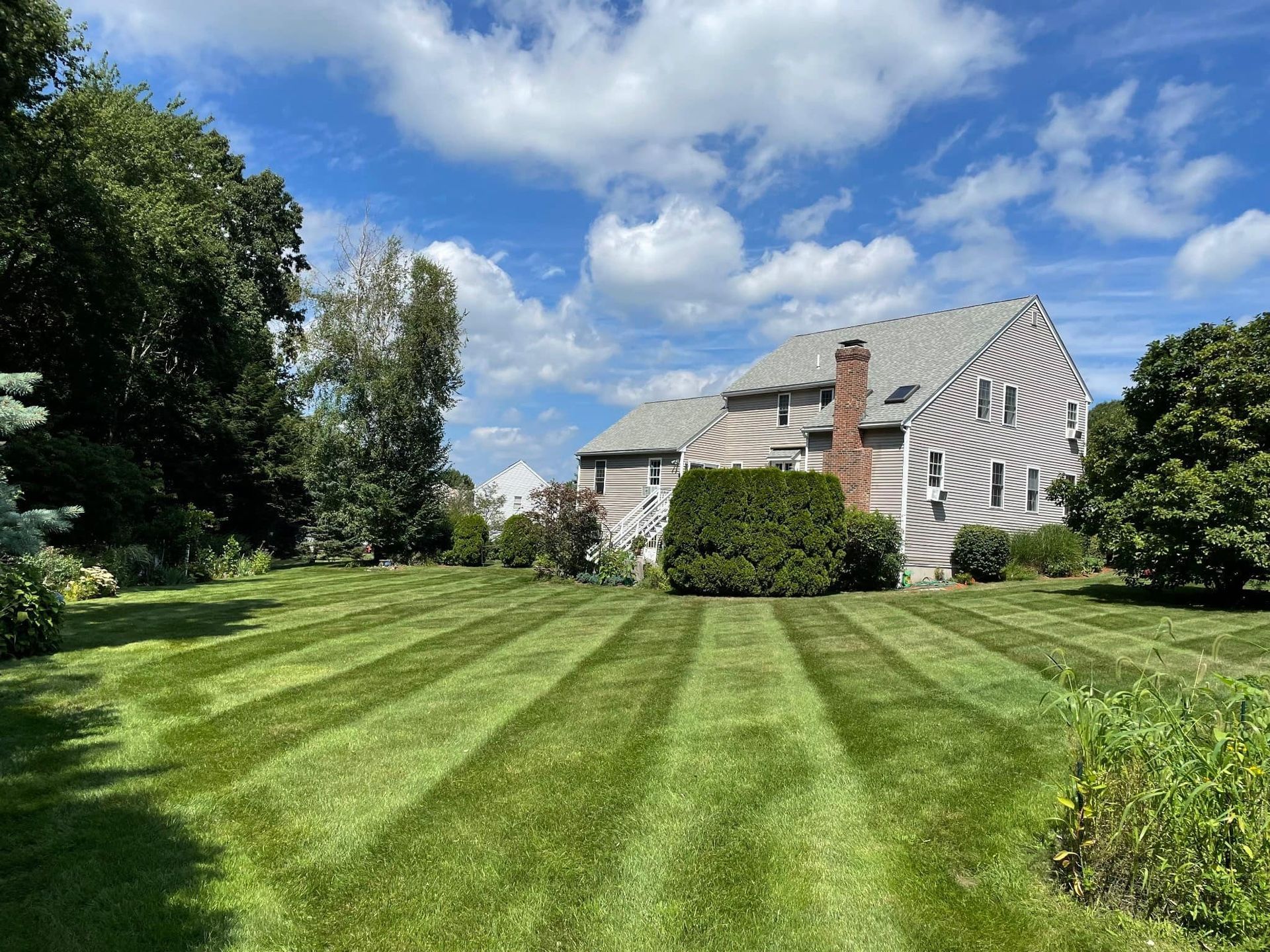 Lawn with striped pattern in front of a house under a cloudy sky.