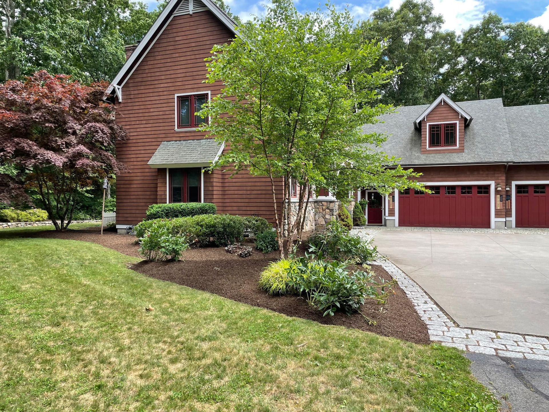 House exterior with red siding and garage, surrounded by landscaping and driveway.