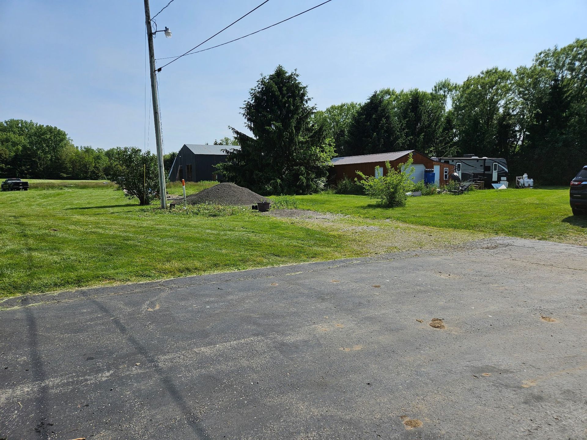 Green lawn with gravel and asphalt leading to buildings and trees under a blue sky.