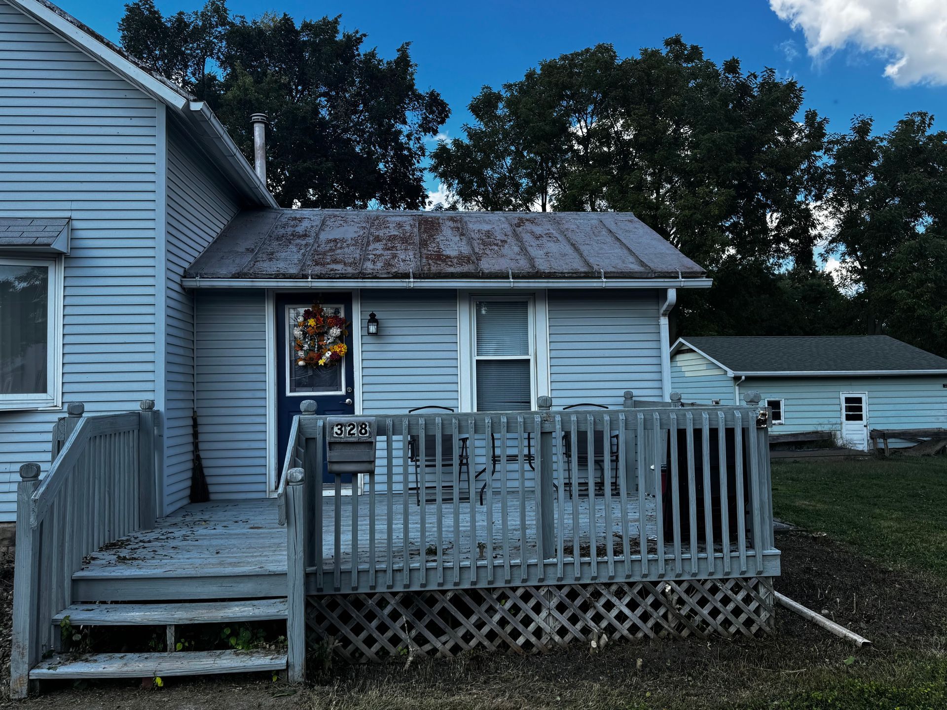 A light blue house with a porch and a small building in the background on a cloudy day.