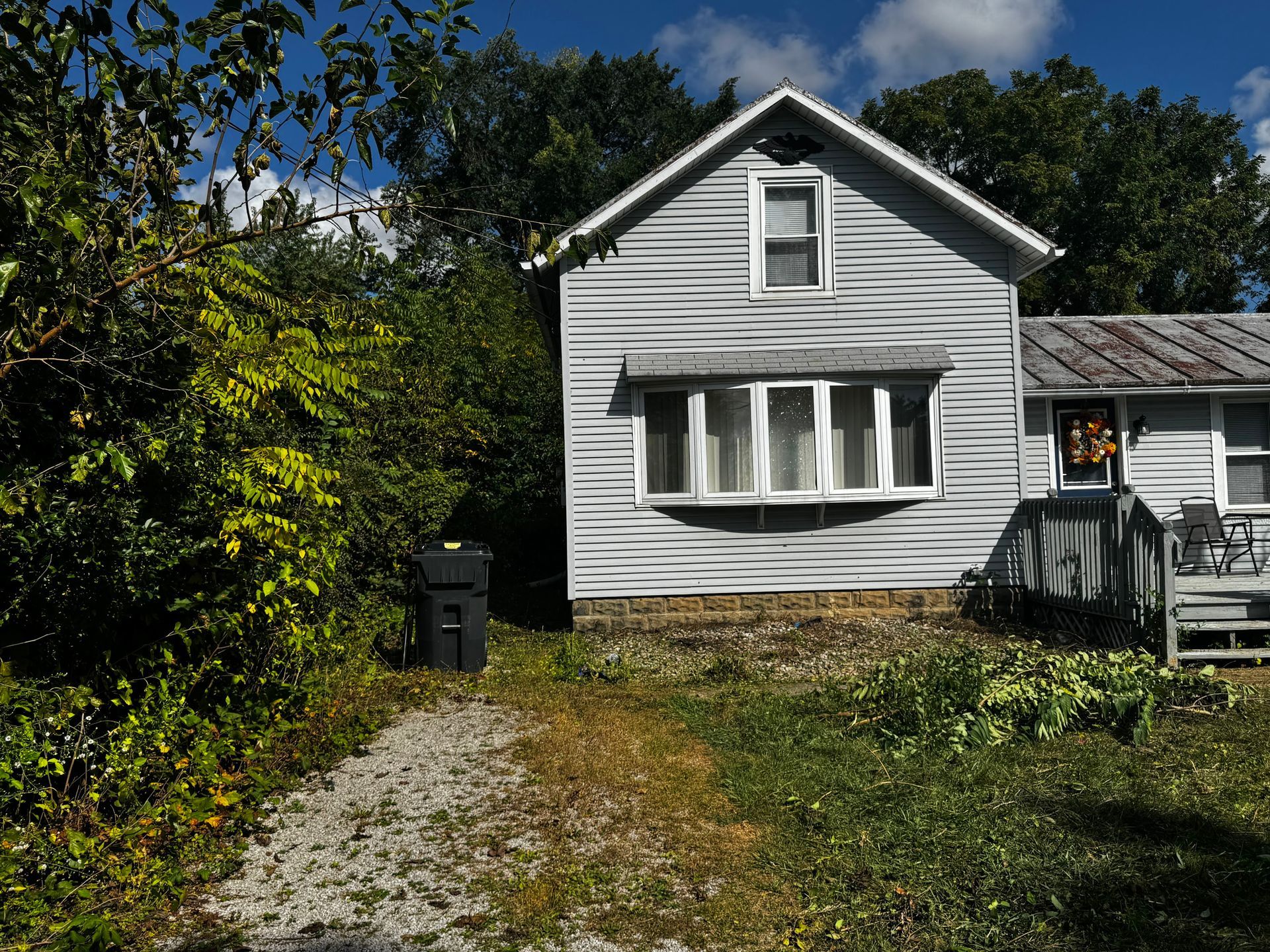 Gray house with bay window and a small porch, gravel path leading to the front door.