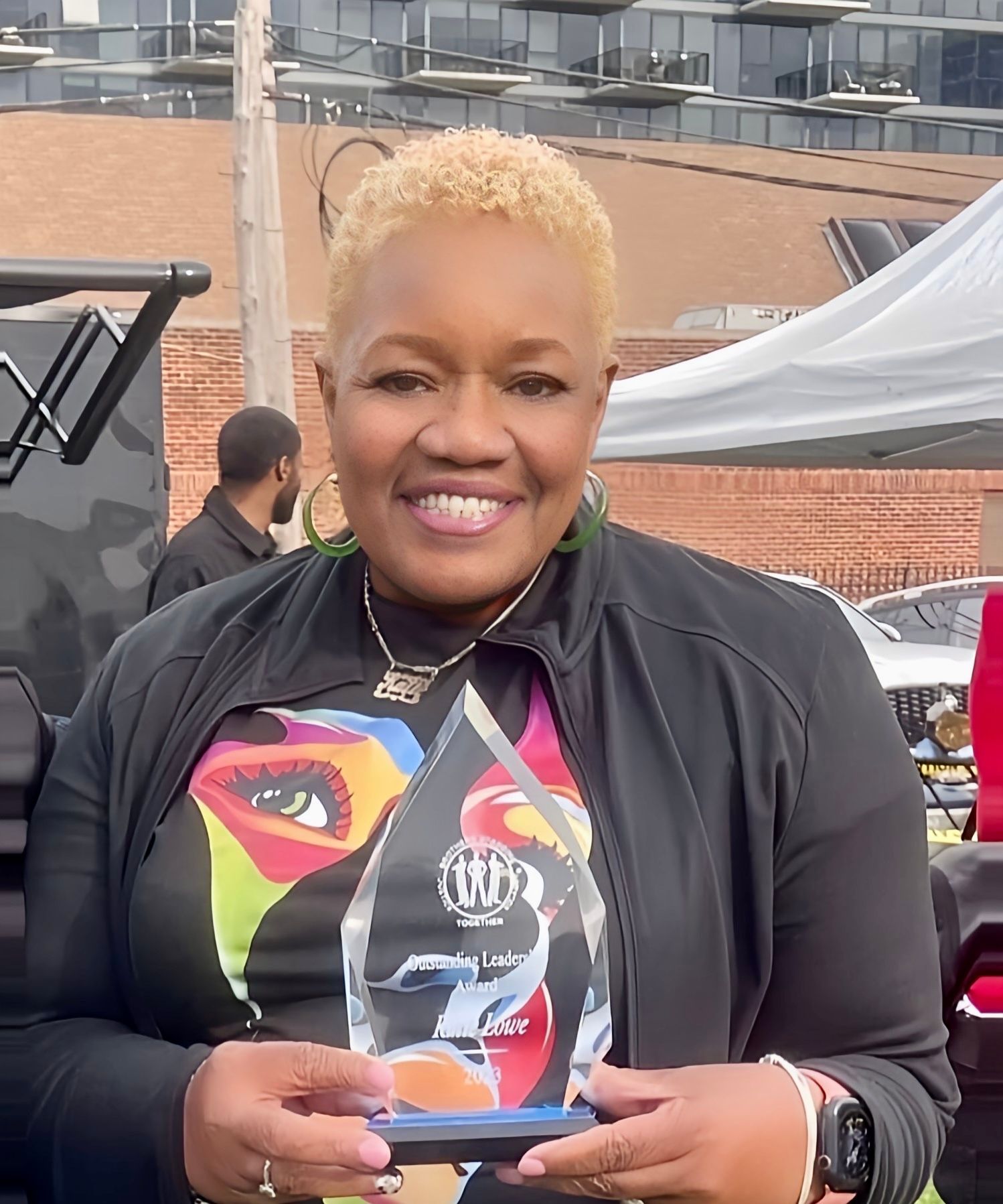 A woman in a black jacket is holding a trophy and smiling.