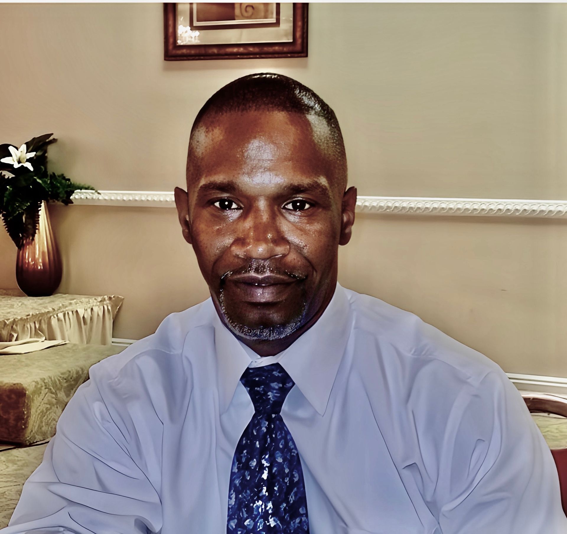 A man wearing a blue shirt and tie looks at the camera