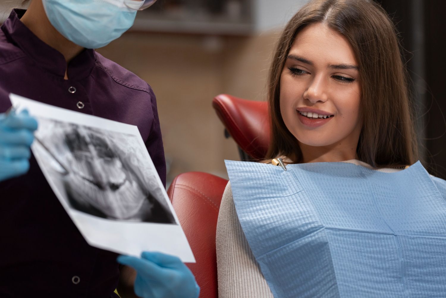 A woman is sitting in a dental chair while a dentist shows her an x-ray of her teeth.