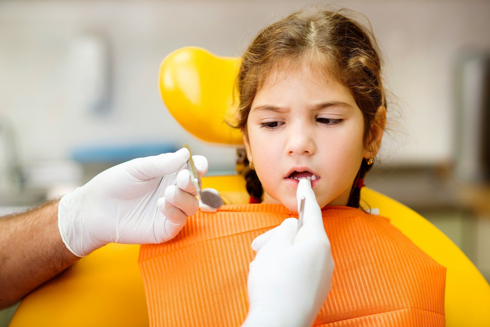 A little girl is sitting in a dental chair while a dentist examines her teeth.