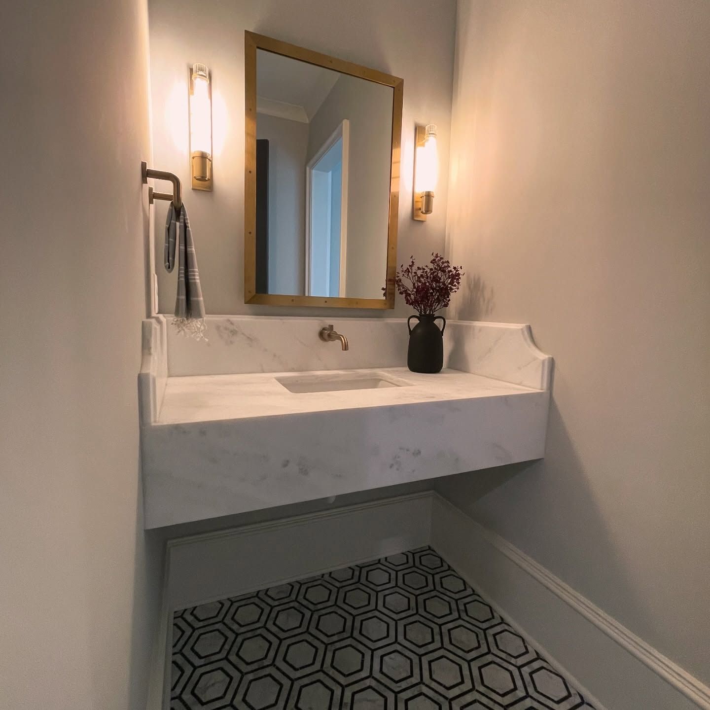 A bathroom with a sink , mirror , and vase of flowers.