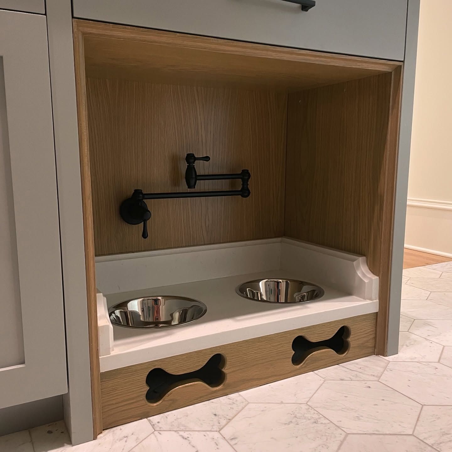 There are two dog bowls with a faucet above them below a cabinet.