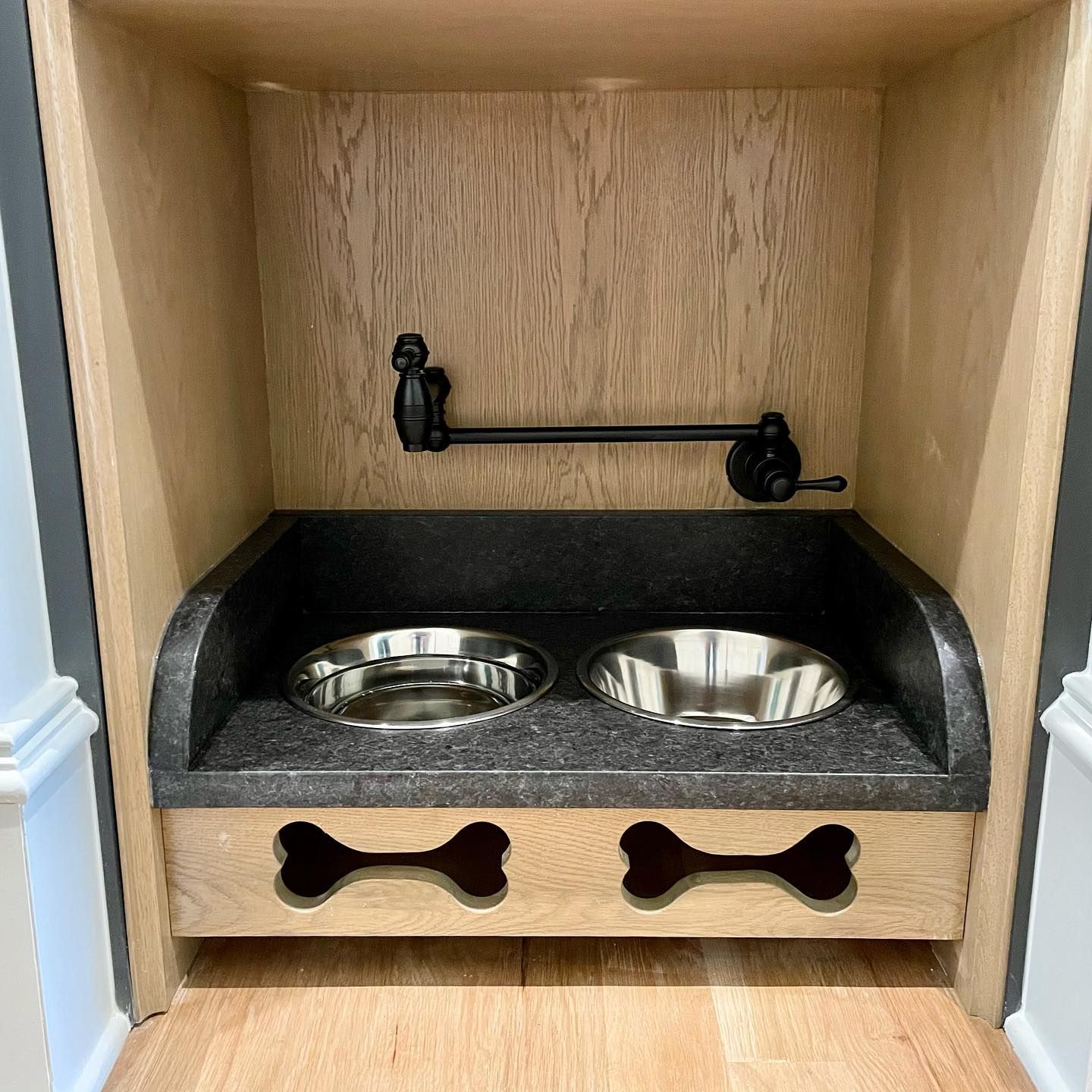 Two stainless steel bowls with a faucet above them are sitting on top of a wooden shelf.