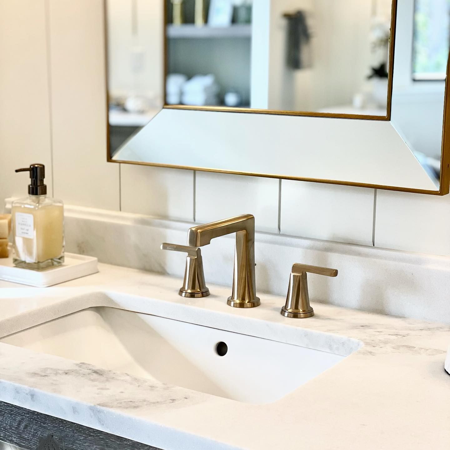 A bathroom sink with a mirror above it and a soap dispenser on the counter.