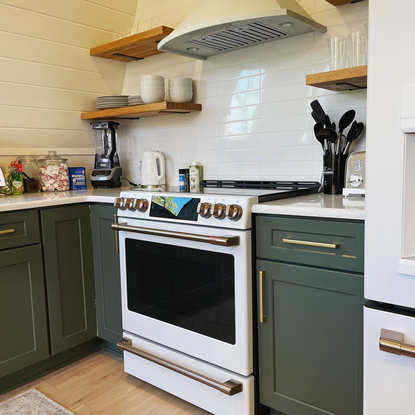 A kitchen with green cabinets , a white stove , and a blender.