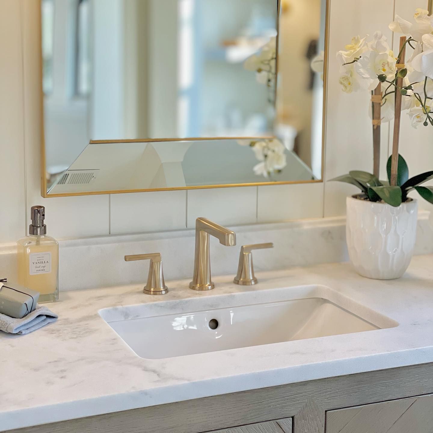 A bathroom sink with a mirror and a vase of flowers.