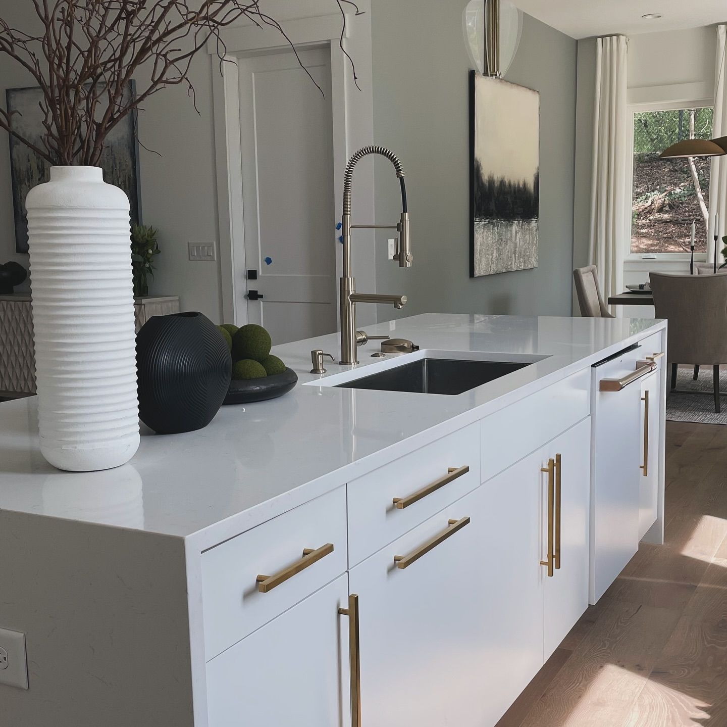 A kitchen with white cabinets and gold handles and a sink